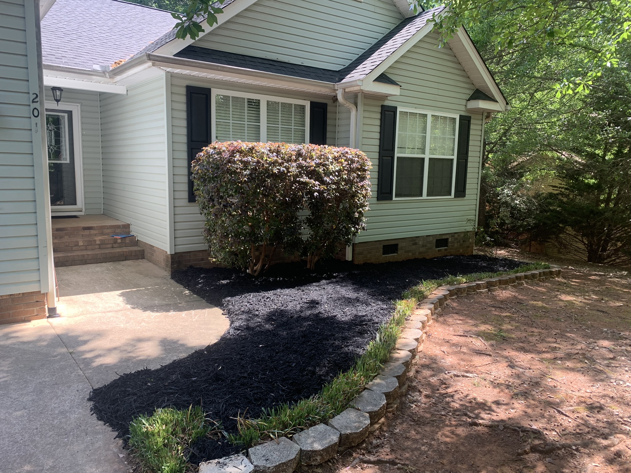 Fresh black mulch bed with stone edging at the front of a house